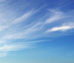 two people standing on the beach flying kites in the blue sky with white wispy clouds