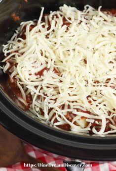 a crock pot filled with meat and cheese on top of a checkered table cloth