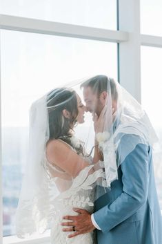 a bride and groom standing in front of a window with their arms around each other