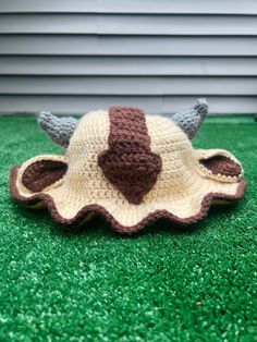 a crocheted hat with horns on it sitting on the grass in front of a house