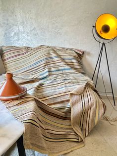 an orange lamp sitting on top of a table next to a bed with a striped blanket