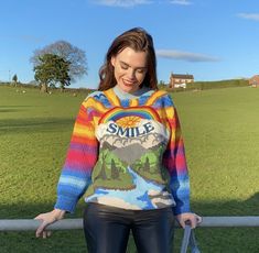 a woman standing in front of a fence wearing a colorful sweater