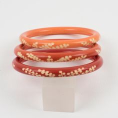 This lovely Galalith bracelet bangle set of three pieces features a chunky spacer domed shape with deep floral carving, all around. A trio of orange variations with peach pink, ginger orange, and orange-red spice colors over a white background.  Measurements for one bracelet: Inside across is 2.44 in diameter (6.2 cm) - outside across is 3.13 in diameter (7.9 cm) - width is 0.32 in (0.8 cm) - width for the three bracelets together is 0.94 in (2.4 cm). The inner circumference of the bracelets is Traditional Orange Bangle Bracelets, Traditional Orange Bangle Bracelet, Handmade Orange Round Bangle, Red Spice, Pink Ginger, Bangle Set, Bracelet Bangle, Peach Pink, Orange Red