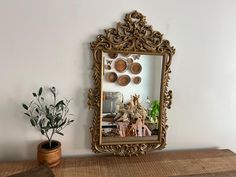 a mirror sitting on top of a wooden table next to a potted plant and vase