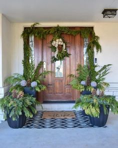 two large planters with pine cones and ferns are on the front steps of a house