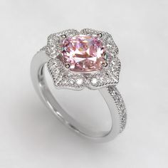 The Platinum Plated Sterling Silver Ring, Cushion Super Light Pink CZ Stone Milgrain Vintage 2 carat Engagement Ring, Pink Diamond Simulant Ring Cocktail Ring (Size 5 to 9) is nothing short of breathtaking. With its vintage-style vibe, it showcases an eye-catching light pink cushion cut cubic zirconia encircled by sparkling round cut accents set in milgrain edge finish petals being formed a heart shape. It would be a sensation at a garden party and a lovely complement to your little black dress Classic Pink Cluster Ring With Center Stone, Elegant Pink Cluster Promise Ring, Classic Pink Cluster Ring With Halo Setting, Classic Pink Cluster Ring For Anniversary, Classic Pink Cluster Ring With Prong Setting, Pink Halo Setting Promise Rings, Classic Pink Topaz Ring For Wedding, Classic Pink Topaz Wedding Ring, Pink Diamond Ring With Halo Setting For Promise