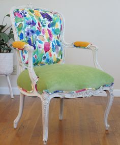 a green chair with floral fabric on the back and arm rests in front of a potted plant