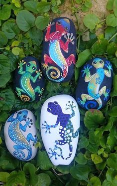 four painted rocks with lizards on them in the grass next to some plants and leaves