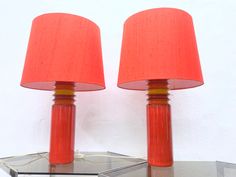 two orange lamps sitting on top of a glass table next to a mirror and lamp shade