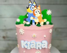 a pink cake with two cartoon characters on top and the word karara spelled in blue