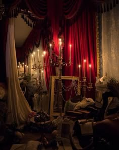 a room with red curtains and candles lit up in the dark, it looks like an old - fashioned bedroom