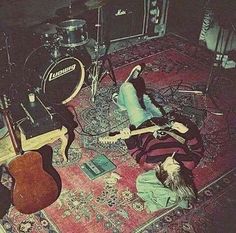 two people laying on the floor in front of guitars and other musical equipment, with one person playing guitar