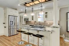 a large kitchen with white cabinets and marble counter tops, two stools at the island