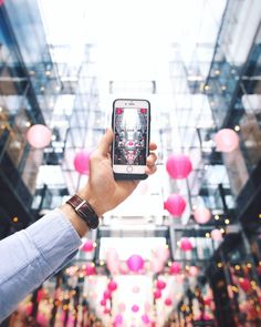 a person holding up a cell phone in front of an indoor mall filled with balloons