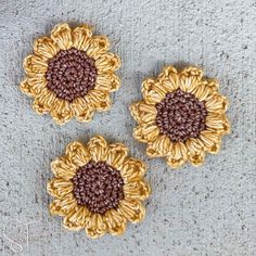 three crocheted sunflowers sitting on top of a cement floor next to each other