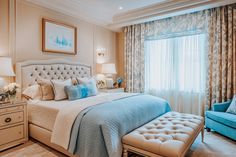 a bedroom with a large bed, blue chair and window in the corner that has curtains on both sides