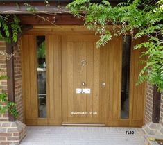 an entrance to a house with two wooden doors and brick pillars, surrounded by greenery