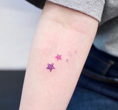 three stars tattoo on the left arm and right arm, with one pink star in the middle