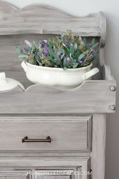 a white bowl filled with flowers sitting on top of a dresser