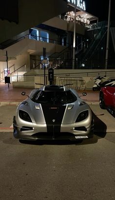 two exotic sports cars parked in front of a building at night with the lights on