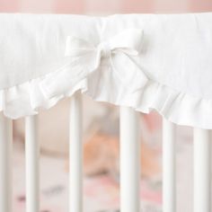 a baby crib with white ruffles and a bow on the front end