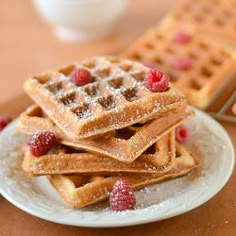 a stack of waffles on a plate with raspberries and powdered sugar