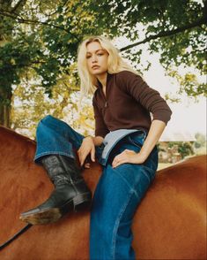 a woman sitting on top of a brown horse next to a green leafy tree