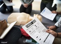 several people sitting on the floor with papers in front of them and one person holding a first aid book