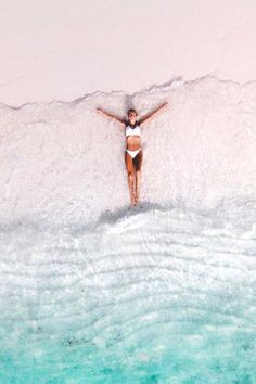 a woman standing in the ocean with her arms spread out and hands behind her back