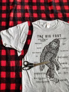 the big foot t - shirt is being cut by a pair of scissors on a red and black checkered blanket