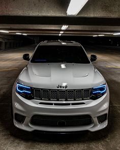 the front end of a white jeep parked in a parking garage with its lights on