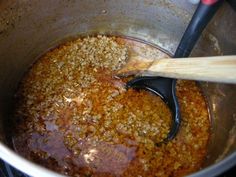 a pot full of food with a wooden spoon in it and someone stirring the mixture