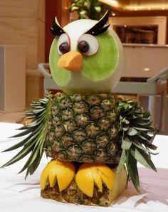 a green bird sitting on top of a pineapple with eyes wide open and tongue out