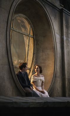 a man and woman are sitting in front of a round window looking into each other's eyes