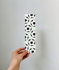 a hand holding up a piece of paper with soccer balls on it and black and white designs