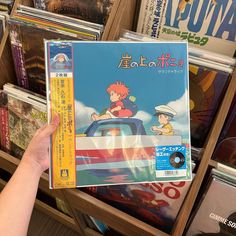 a person holding up a cd in front of a book shelf filled with books and cds