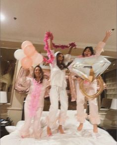 three women standing on top of a bed with balloons and streamers in the air