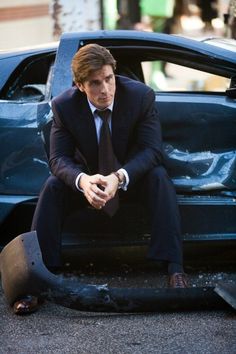 a man in a suit sitting on the hood of a car