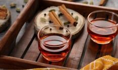 two glasses of tea sit on a wooden tray with cinnamons and spices in the background