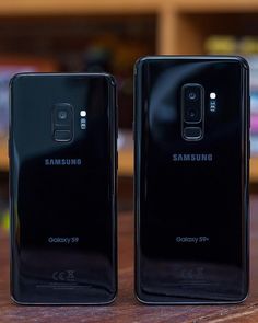 two samsung phones sitting side by side on a wooden table in front of a bookcase