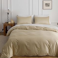 a bed with beige sheets and pillows in a white room next to a lamp on a table