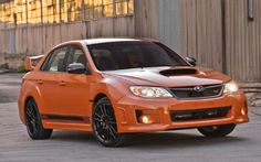 an orange subarunt is parked in front of a building with windows and doors