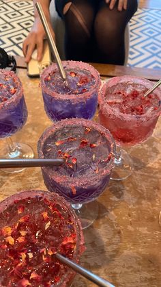 four glasses filled with liquid sitting on top of a wooden table next to a woman