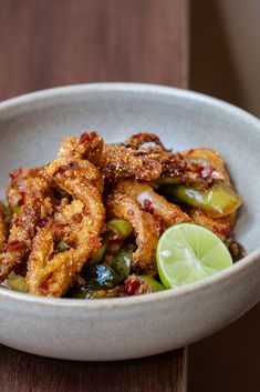 a white bowl filled with fried food and garnished with lime wedges on the side