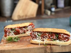 two meatball sub sandwiches sitting on top of a cutting board next to each other