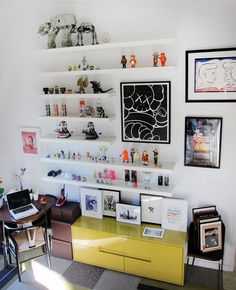 there is a desk and shelves in the room with many pictures on the wall above it