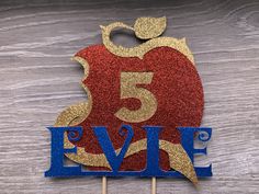 a cake topper with the number five in blue and gold glitter, on a wooden table