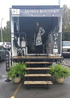 a woman is standing in the doorway of a mobile boutique with stairs leading up to it