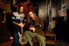 two men sitting next to each other holding guitars