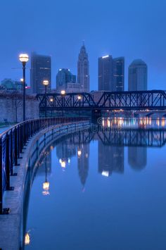 the city skyline is lit up at night with lights reflecting in the water and buildings on either side